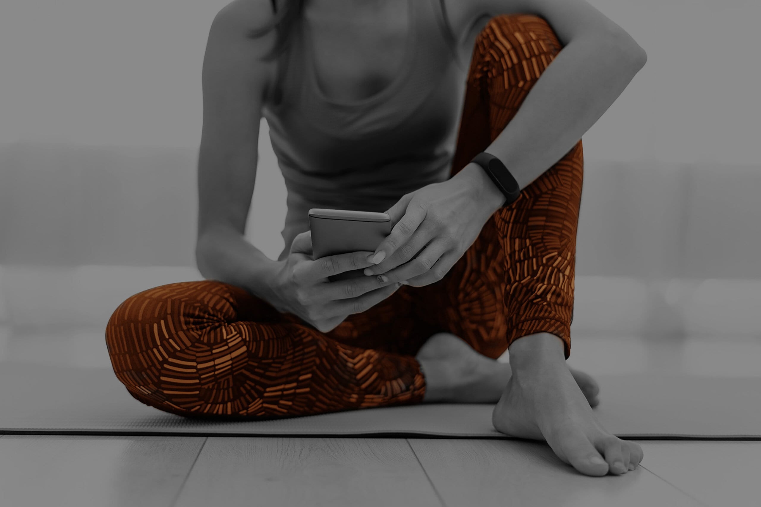 Young sporty woman using smartphone, sitting on fitness mat